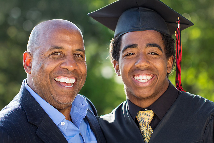 Up close portrait of a father and son smiling as the son wears graduation cap