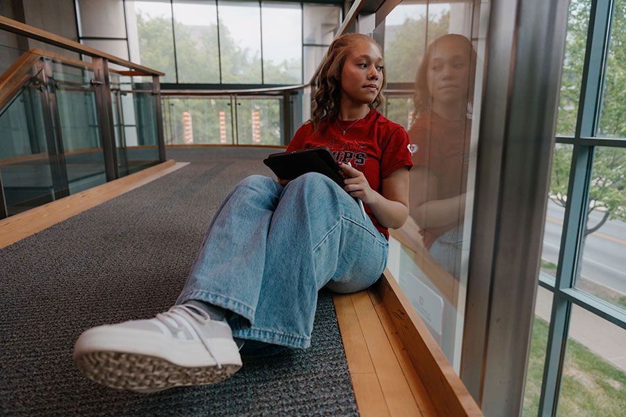 IU student Amyana Moody looking out the window of a campus building while working on a tablet