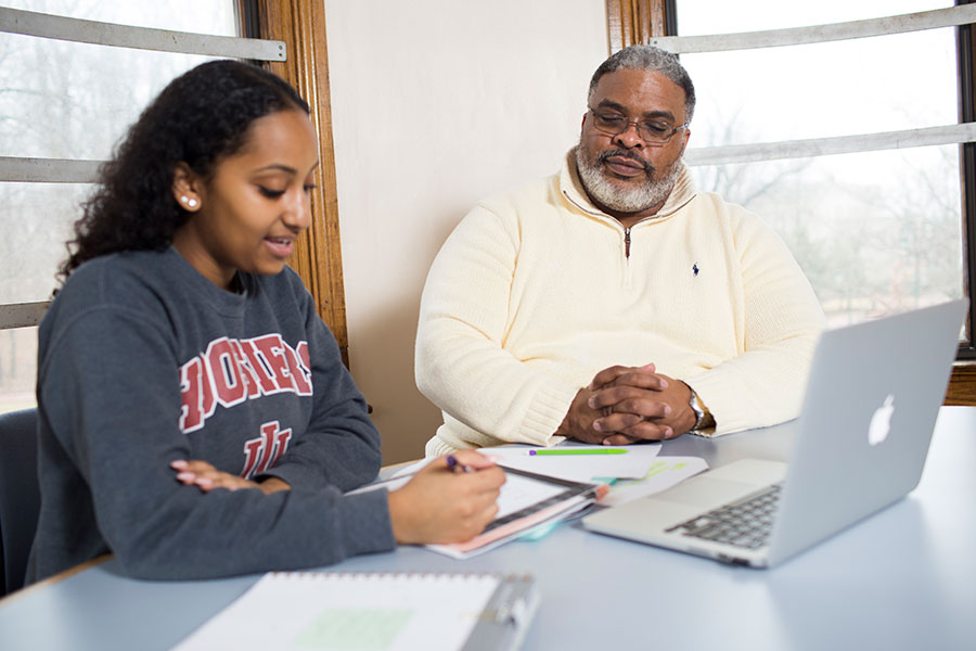 A student (L) sitting at a table with Groups Scholars Program Director Samuel Young III (R) as they review academic notes