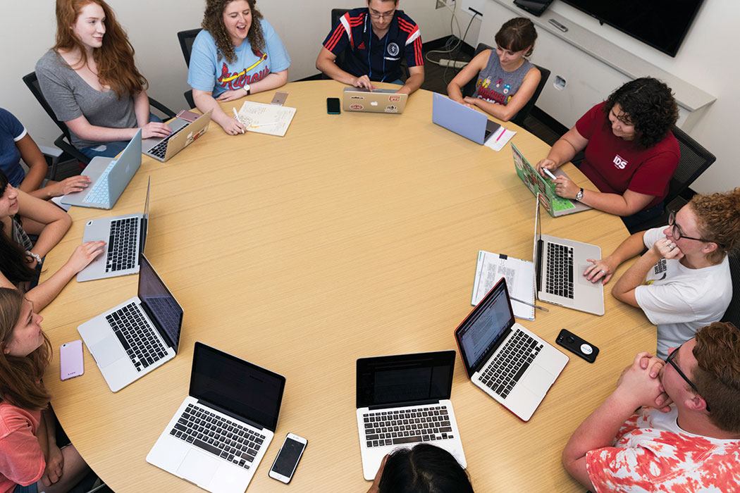 A full-color photo shows students gathered around a table, a laptop (and sometimes also a smartphone) in front of each of them.