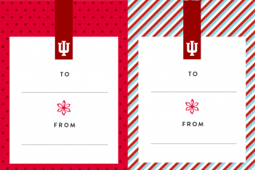 Two horizontal gift tags next to each other. Both tags feature a bold crimson tab with a white IU trident at the top, and a red snowflake on a white background with blank To and From lines in the center. The tag on the left features a border of light crimson with dark crimson polka dots. The tag on the right features a border of diagonal white, dark crimson, and aqua stripes.