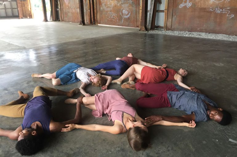 A group of dancers lie in a circle on the floor of the mill