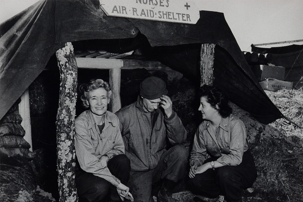 Pyle and two nurses crouch in an entrenched air raid shelter in this black-and-white photo.