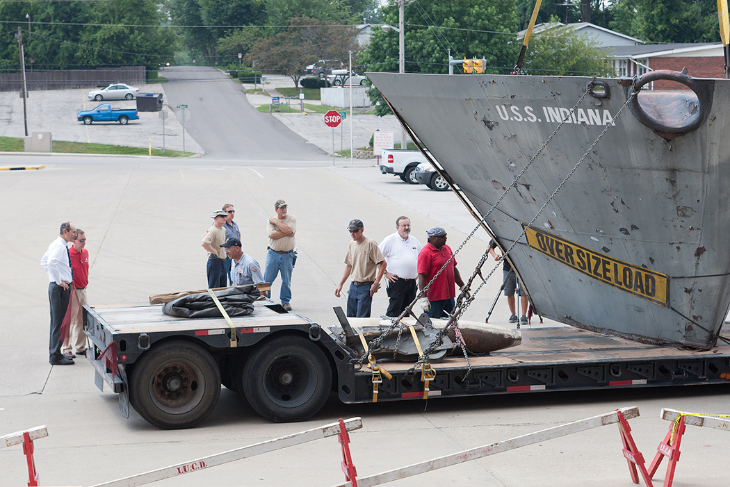 Bearing an "OVERSIZE LOAD" sign, the prow of the USS Indiana arrives at Memorial Stadium on a flatbed truck.