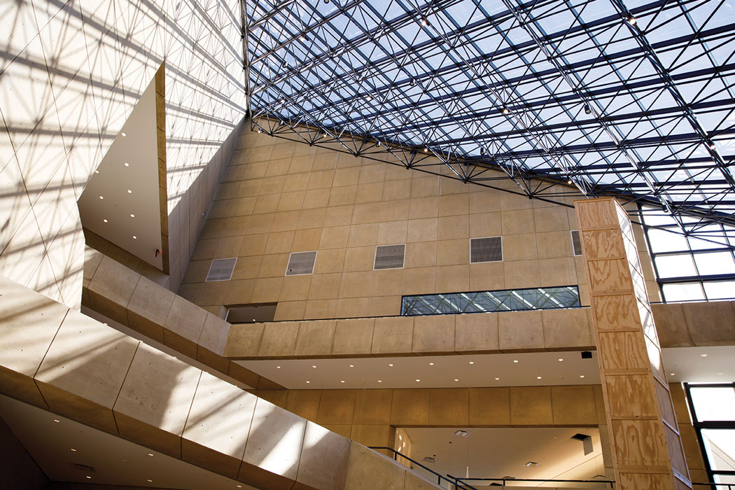 Light shines through a ceiling of windows into an angular, stone-surfaced atrium.