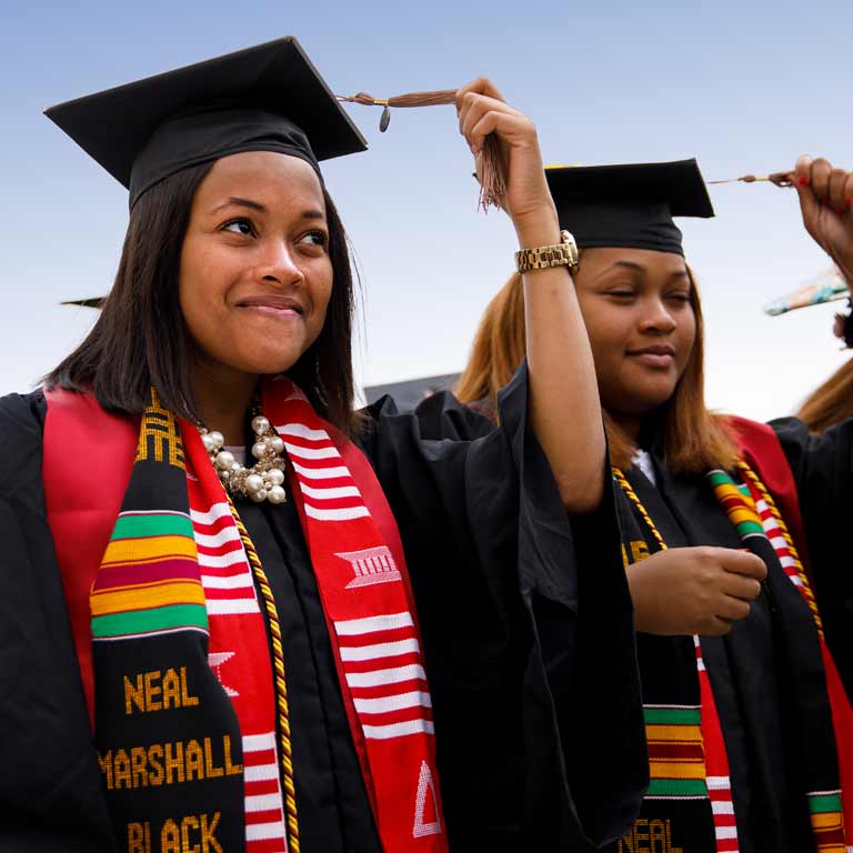 Two IU students wearing Neal Marshall Black Culture Center stoles over their graduation gowns turn the tassels on their mortarboards