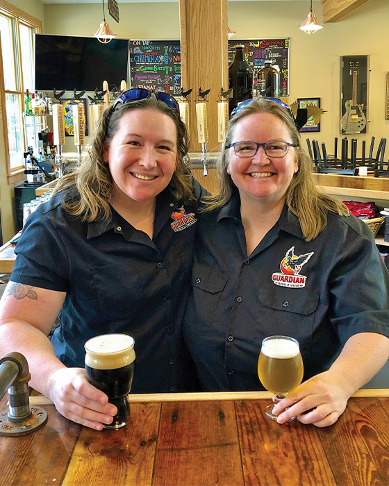 Kim Collins and Kate Bishop stand behind Guardian Brewing Company bar with beer in hand