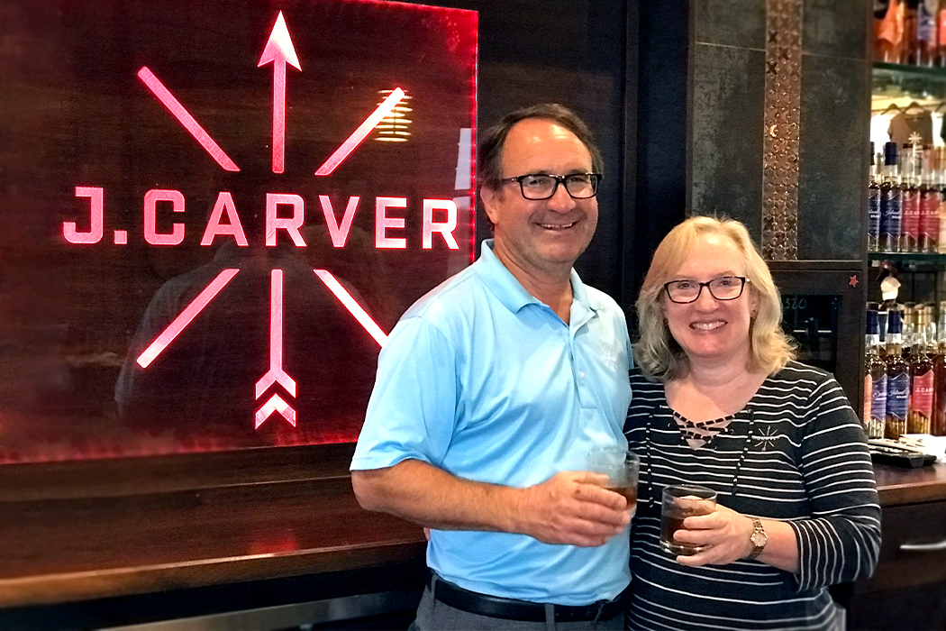Bill Miller and wife stand at J. Carver bar and hold drinks 