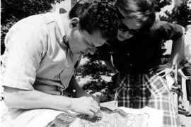 In this black-and-white photo, a male student and female student hunch over a campus map to study their whereabouts.