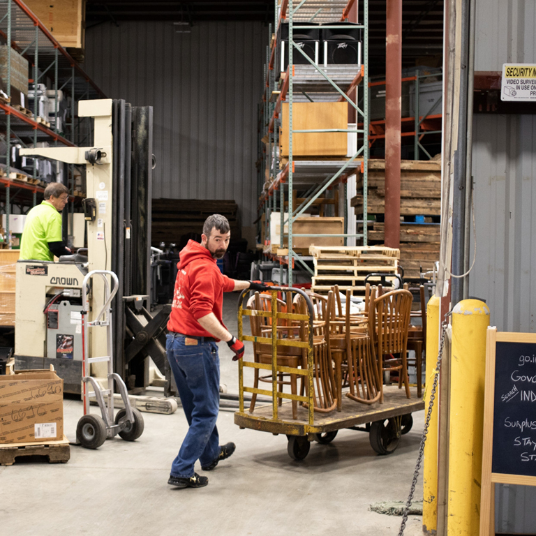 Two people in a warehouse moving furniture.