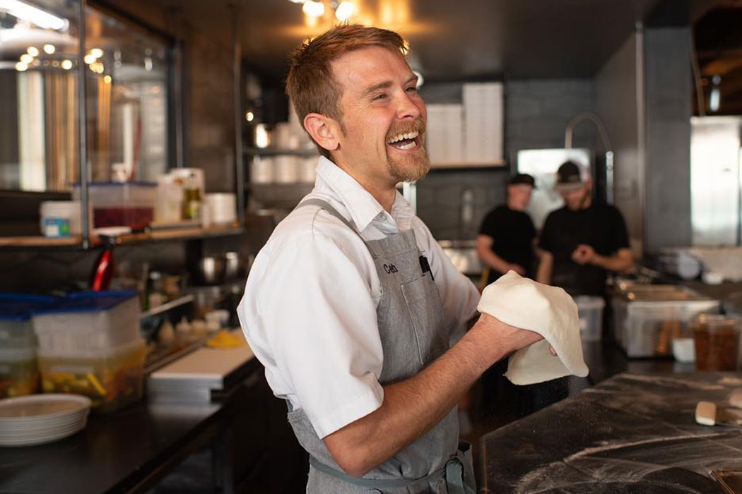 Caleb Schiff smiles while tossing pizza dough 