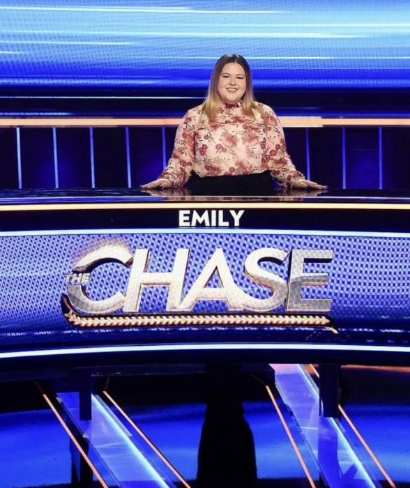 Woman standing behind a desk on a game show set.