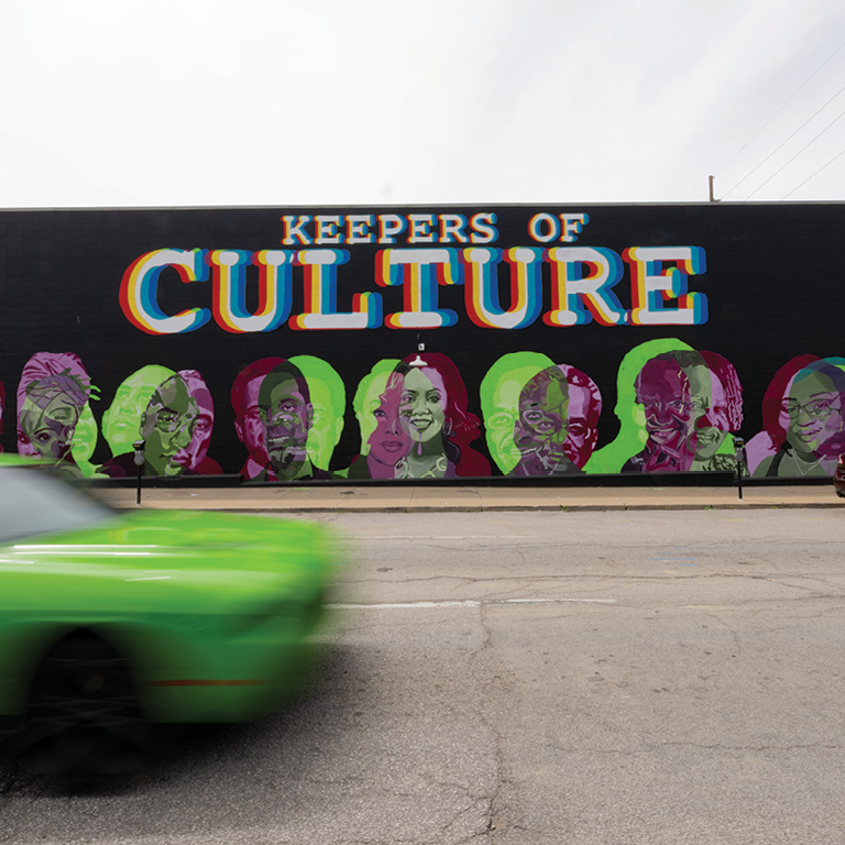 A mural painted on a building exterior features the words "Keepers of Culture" at top; portraits of Black figures feature at bottom.