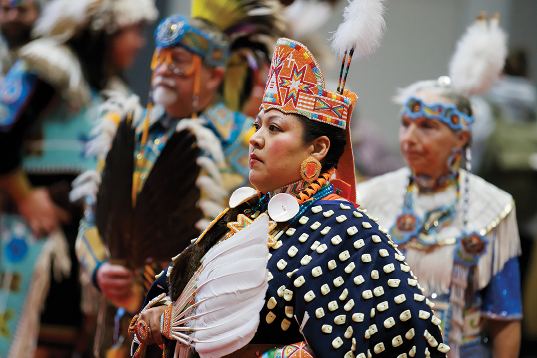 A person in powwow regalia that includes an intricately beaded headpiece in bright orange, red, blue, and yellow. 