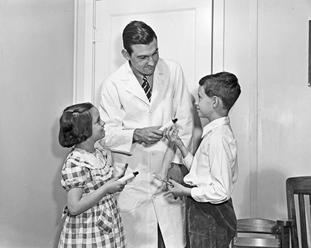 IU alum and Crest founder Joseph Charles Muhler hands children toothpaste at his dentistry office. 