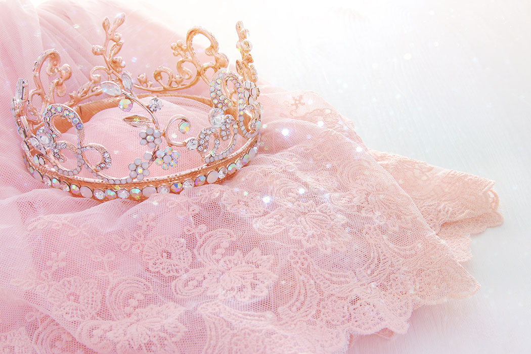 A diamond princess crown lays atop pink lace fabric