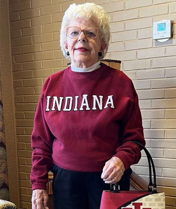 Eleanor Cox Riggs stands wearing her favorite crimson IU sweater and an IU purse, ready to cheer for the Hoosiers at her retirement home.