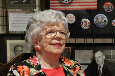 Eleanor Cox Riggs smiles in front of her political button collection in a local museum.