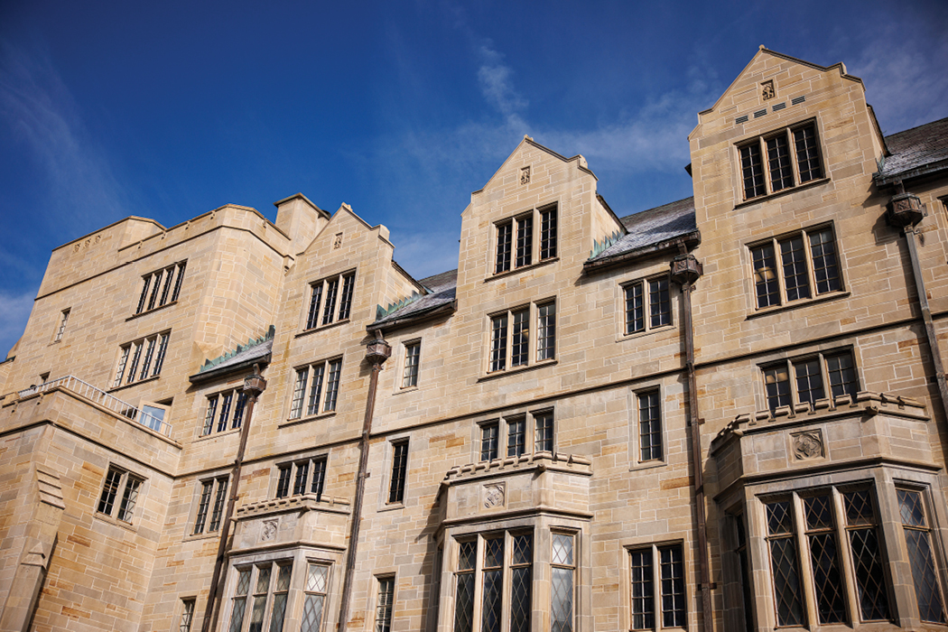 This photo of Morrison Hall was taken at ground level, looking up at the five-story, limestone building. The building is set against a bright blue, partly cloudy sky.