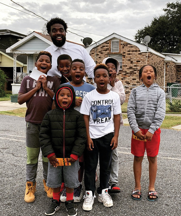 Russell Ledet stands with a group of children, expressing excitement and glee, in front of brick homes in Ledet's childhood neighborhood.